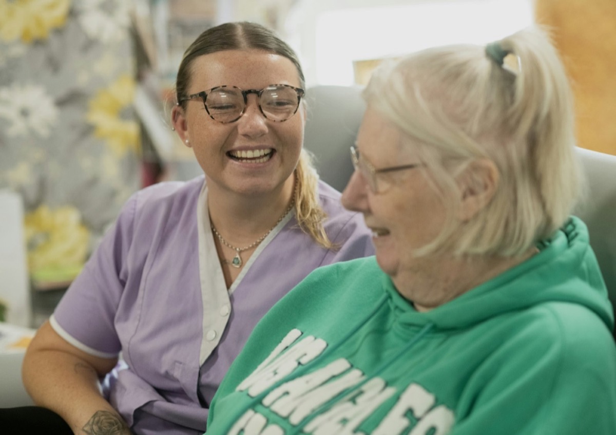 A support worker and an older woman laughing together
