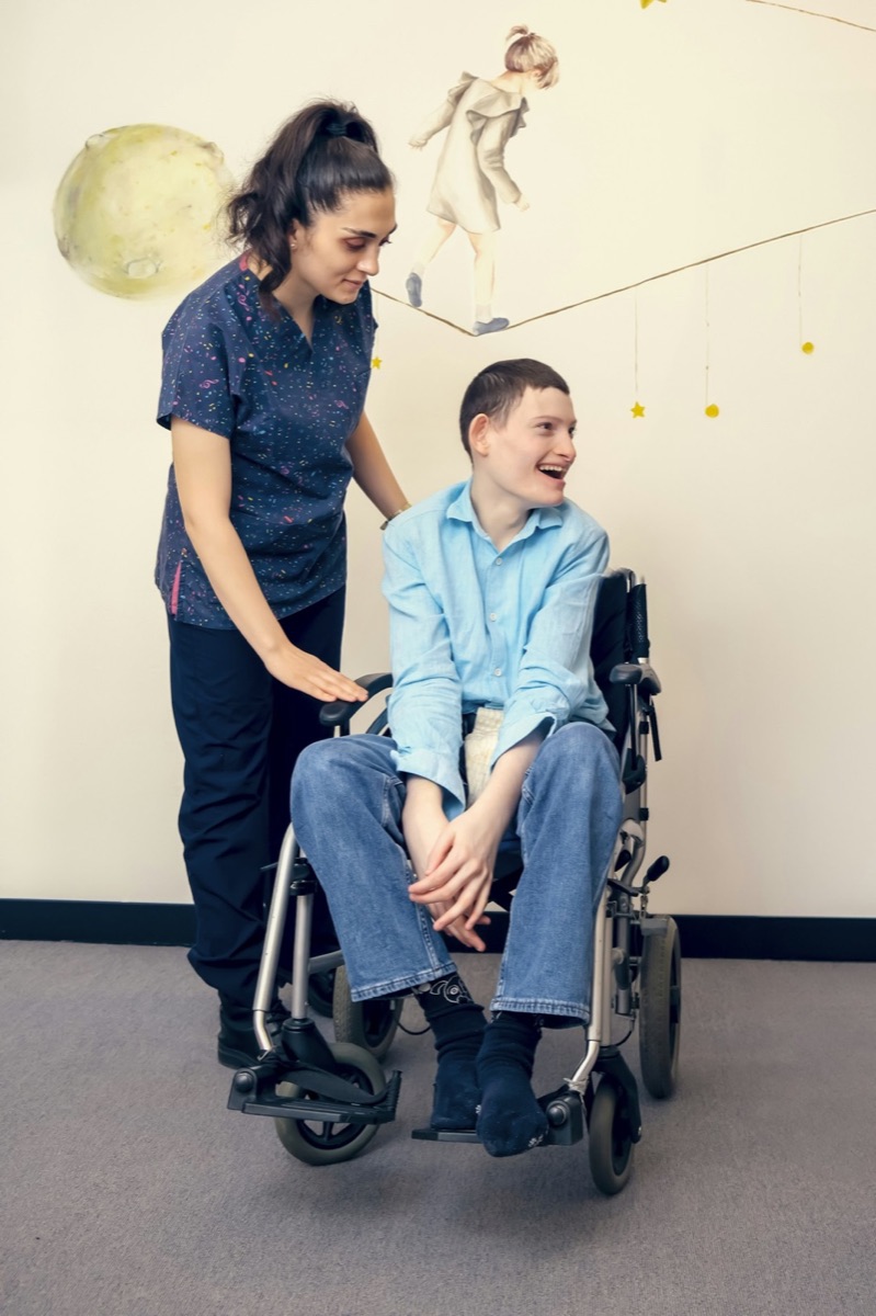 A support worker standing beside a smiling young man in a wheelchair